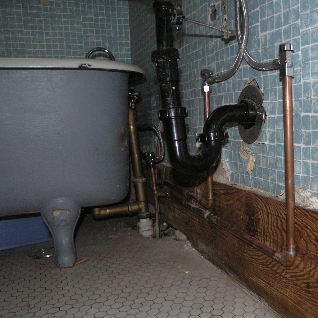 Exposed copper and PVC pipework behind a bathroom wall
