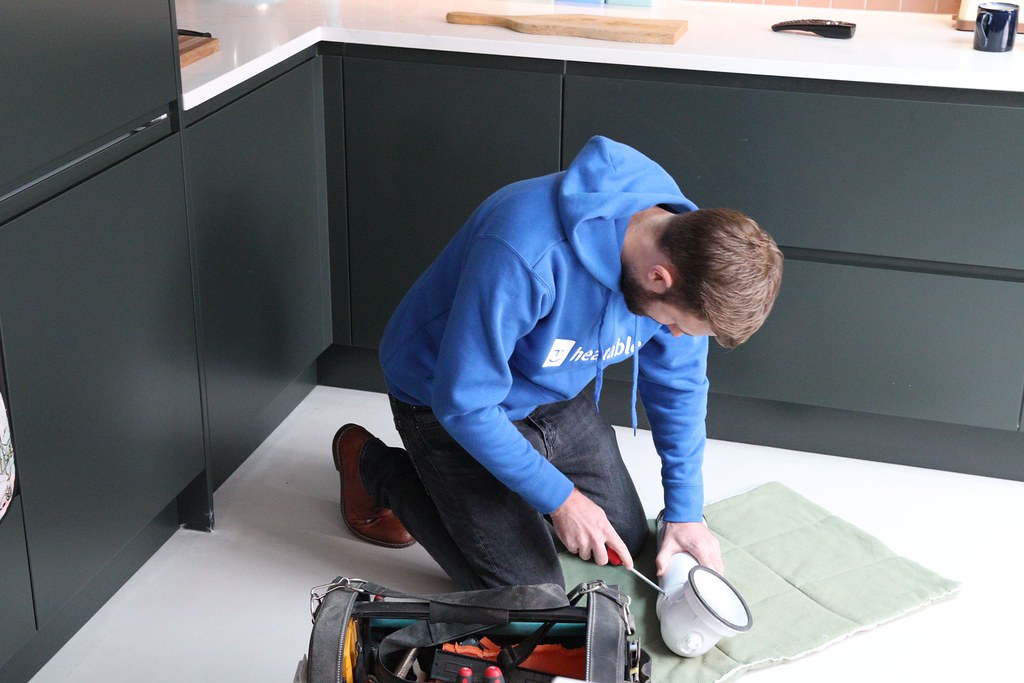 Plumber kneeling at work on a kitchen installation with tools laid out